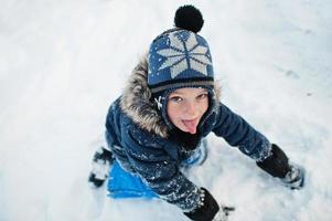 Boy show tongue in winter nature. Outdoors in snow. photo