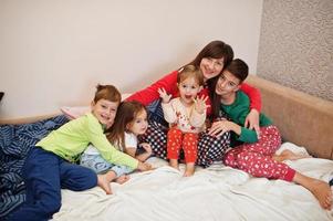 la gran familia feliz se está divirtiendo juntos en el dormitorio. gran concepto de mañana familiar. madre con cuatro hijos usa pijama en la cama en casa. foto