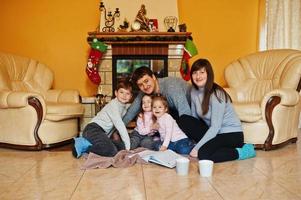 feliz joven familia numerosa en casa junto a una chimenea en una cálida sala de estar el día de invierno. foto