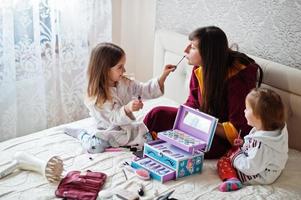 madre e hijas maquillándose en la cama del dormitorio. foto