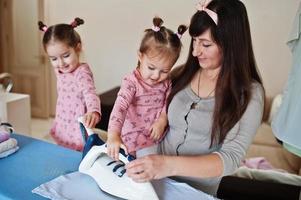 mujer madre y sus dos hijas niñas como pequeñas ayudantes planchando en casa. foto