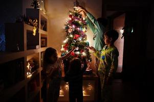 Kids looking on Christmas tree with shining garlands on evening home. photo