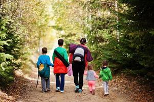 Back of mother with four kids walking on wood mountains. Family travel and hiking with childrens. Wear backpack. photo
