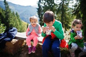 Three kids resting in mountains and drink juice from stick pack sachet. Travel and hiking with childrens. photo