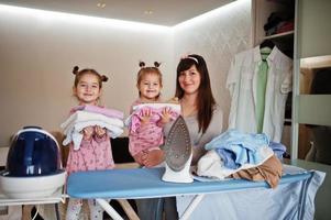 mujer madre y sus dos hijas niñas como pequeñas ayudantes planchando en casa. foto