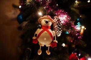 Snowman on Christmas tree with shining garlands on evening home. photo