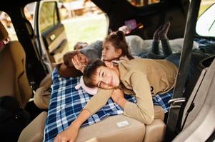 familia de cuatro hijos en el interior del vehículo. niños en el baúl. viajar en coche, mentir y divertirse, concepto de ambiente. foto