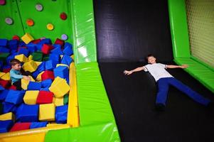 Two brothers lying on pool with colored foam cubes and trampoline in indoor play center. photo