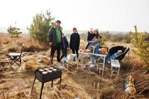 familia numerosa con cuatro niños haciendo barbacoas en una terraza en el bosque de pinos. día de barbacoa con parrilla. foto