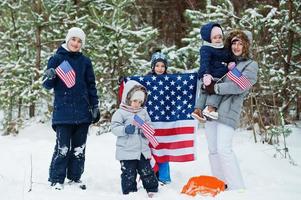 Family with four kids holding flag of USA on winter landscape. photo