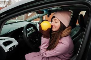 Young woman sit in car and sniffs a lemon at winter. photo