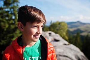 Boy on top of mountain. Children hiking on beautiful day in mountains, resting on rock and admire amazing view peaks. Active family vacation leisure with kids.Outdoor fun and healthy activity. photo