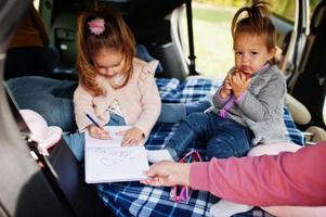 Mother with two daughter kids at vehicle interior. Children in trunk. Traveling by car, lying and having fun, atmosphere concept. photo