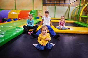 niños jugando en el centro de juegos interior y sentados en un trampolín. familia numerosa con cuatro hijos. foto