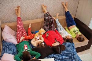 la gran familia feliz se está divirtiendo juntos en el dormitorio. gran concepto de mañana familiar. madre con cuatro hijos usa pijama en la cama en casa. foto