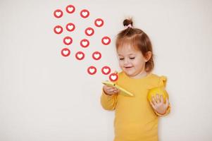 Baby girl in yellow with lemon and mobile phone with heart emoji, isolated background. photo