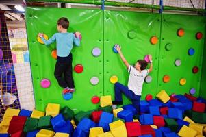 Two brothers kids climbing on a green wall in attraction playground. photo