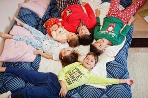 la gran familia feliz se está divirtiendo juntos en el dormitorio. gran concepto de mañana familiar. madre con cuatro hijos usa pijama en la cama en casa. foto