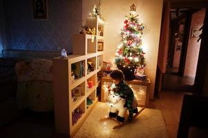 Baby girl on rocking cow toy against Christmas tree with shining garlands on evening home. photo