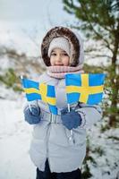 Scandinavian baby girl with Sweden flag in winter swedish landscape. photo