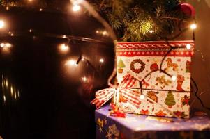 Gift box against Christmas tree with shining garlands on evening home. photo