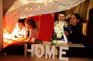 Playing kids with kitty in tent at night home. Hygge mood. photo