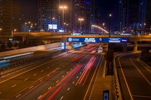 larga exposición de automóviles en movimiento en la carretera nocturna en dubai. vida nocturna en el puerto deportivo de dubai. foto