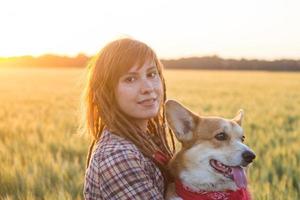 Una joven mujer feliz con rastas juega con un perro corgi en los campos de trigo de verano foto