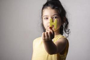 linda niña con letra h en la mano con un vestido amarillo foto