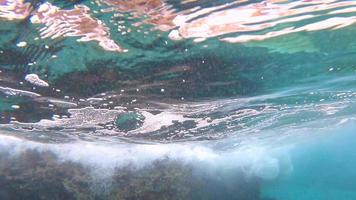o ângulo subaquático das ondas do oceano azul tropical quebrando no recife. respingo de espuma e ondas batendo em uma superfície rochosa. video