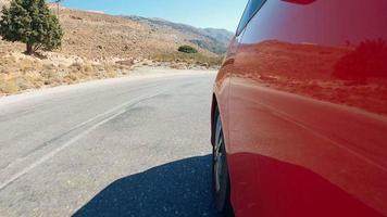 Red car speeds down scenic switchback road running through the idyllic curve mountain road. Sport car drive a challenging serpentine route leading through the stones in Greece.