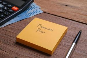 Pen, glasses, banknotes and yellow sticky notes written with Financial Plan on wooden background photo