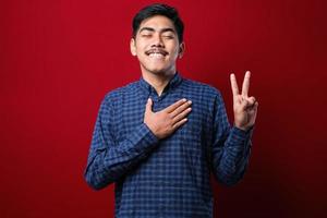 Young handsome asian man wearing casual shirt smiling swearing with hand on chest and fingers up, making a loyalty promise oath photo