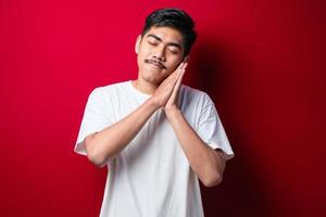 Asian handsome man wearing white tshirt sleeping tired dreaming and posing with hands together while smiling with closed eyes photo