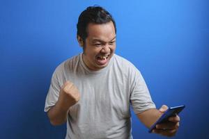 Fat Asian guy wearing a gray T-shirt looks happy over the good news he received from his smartphone photo
