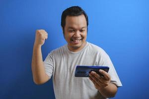 Fat Asian guy wearing a gray T-shirt looks happy over the good news he received from his smartphone photo