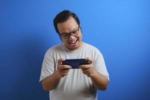 photo of a fat Asian man wearing a gray T-shirt looking happy playing a game on his smartphone