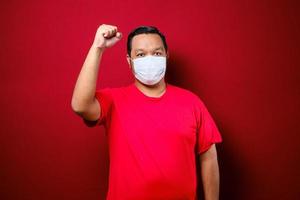 Young asian man wearing a medical face mask while raise his hand up to encourage and protects against the spread of corona virus disease photo