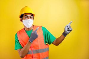 Asian construction worker wearing protective mask pointing isomething in his side photo