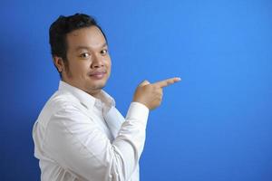 Portrait of Asian young happy office worker smiling and pointing to presenting something on his side photo