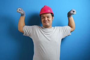 Portrait of funny fat Asian man wearing red helmet smiling proudly while showing double biceps pose, strength over confidence concept photo