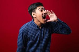 Young asian man wearing casual shirt style shouting and screaming loud to side with hand on mouth photo