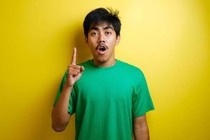 Asian young man in green t-shirt looked happy thinking and looking up, having good idea photo