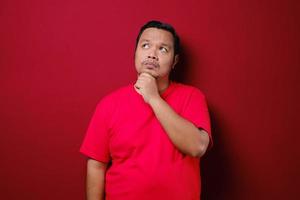 A portrait of a young asian man thinking looking up isolated over red background photo