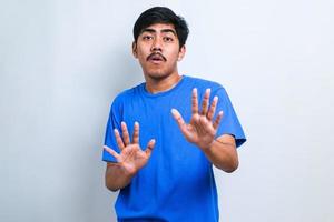 Asian man moving away hands palms showing refusal and denial with afraid and disgusting expression. Stop and forbidden. photo