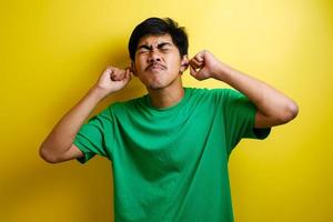 joven asiático con camiseta verde cierra los oídos con ambas manos foto