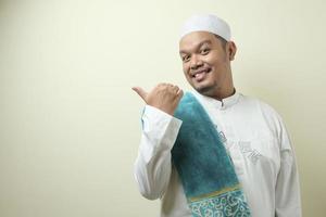 Portrait of Asian young muslim man smiling and pointing to presenting something on his side photo