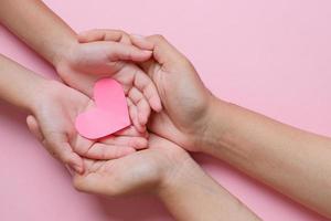 manos de adultos y niños con corazón rojo sobre fondo rosa. amor, salud, familia, seguro, concepto de donación