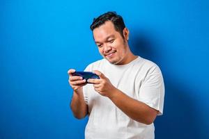 Funny Fat Asian Guy Playing Games on Tablet Smart Phone against blue background photo