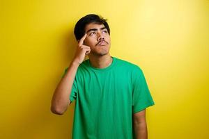 Asian young man in green t-shirt looked happy thinking and looking up, having good idea photo